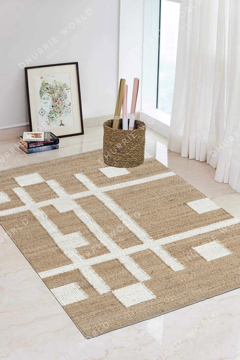 May include: A beige and white geometric patterned jute rug with a white background and beige lines. The rug is on a white tiled floor in a room with a white wall and a wicker basket.