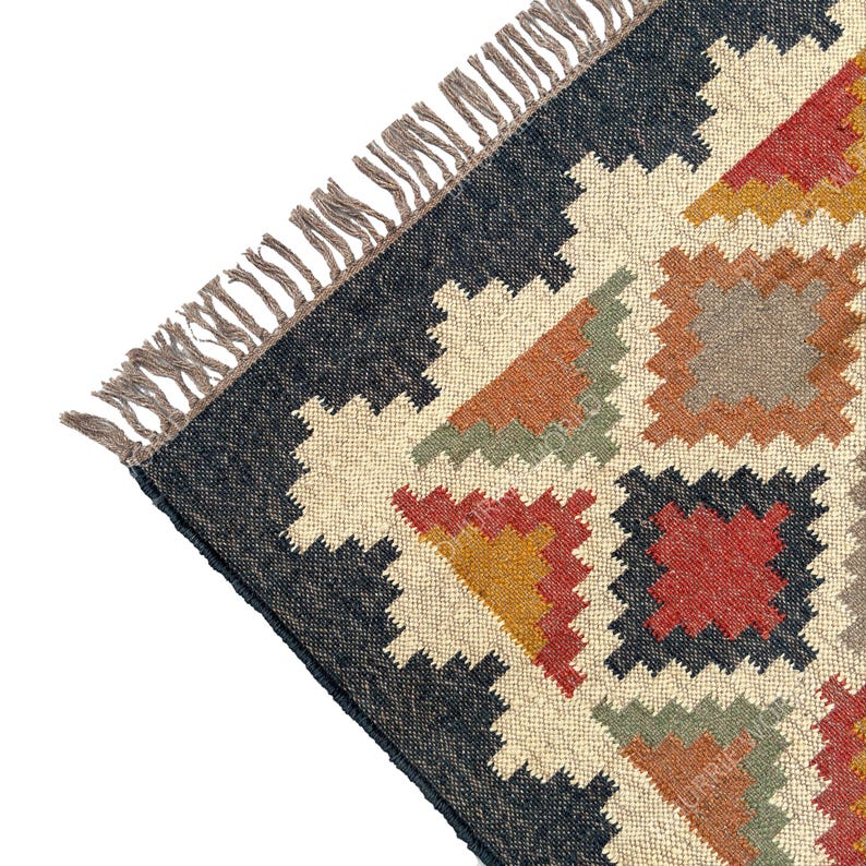 May include: A close-up of a colorful rug with a geometric pattern. The rug is made of natural fibers and has a fringe border. The colors in the rug are black, white, red, orange, yellow, and green.