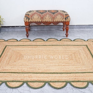 May include: A natural fiber rug with a green border and scalloped edges. The rug has a woven texture and is made of jute. The rug is placed on a gray tiled floor.
