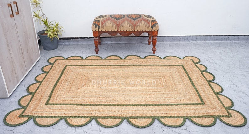May include: A natural fiber rug with a green border and scalloped edges. The rug has a woven texture and is made of jute. The rug is placed on a gray tiled floor.