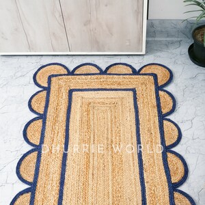 May include: A natural fiber rug with a rectangular shape and a scalloped border. The rug has a dark blue trim around the edges and a light brown color.