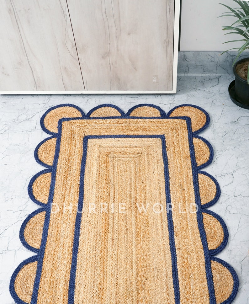 May include: A natural fiber rug with a rectangular shape and a scalloped border. The rug has a dark blue trim around the edges and a light brown color.