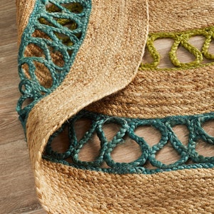 May include: A round jute rug with a teal and green border. The rug's natural tan color is complemented by the teal and green accents, creating a textured and decorative floor covering. The border features an open, braided design.