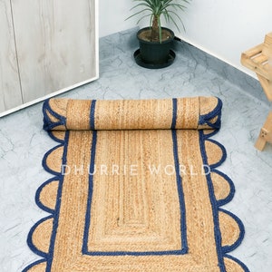 May include: A natural fiber rug with a scalloped edge and a blue border. The rug is rolled up in the image. The text "DHURRIE WORLD" is visible on the rug.