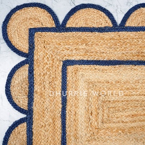 May include: A natural fiber rug with a square shape and a scalloped border. The rug has a dark blue trim around the edges and a smaller square in the center. The text "DHURRIE WORLD" is visible in the center of the rug.