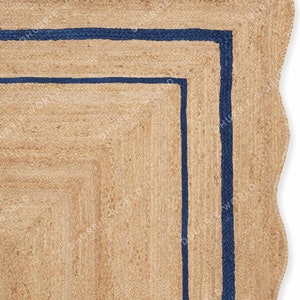 May include: A natural fiber rug with a wavy edge and a double border of dark blue. The rug is made of jute and has a natural, earthy color.