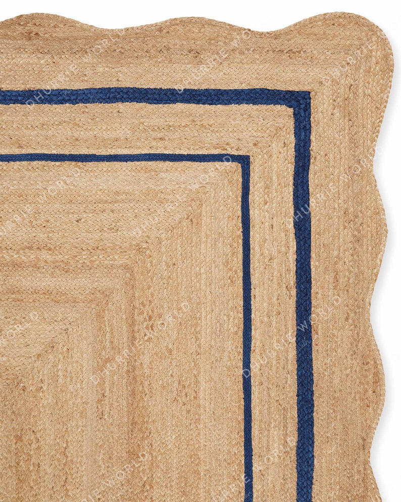 May include: A natural fiber rug with a wavy edge and a double border of dark blue. The rug is made of jute and has a natural, earthy color.