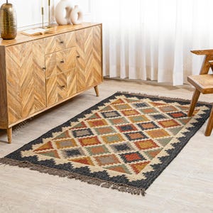 May include: A black and brown patterned jute rug with fringe. The rug has a geometric design with diamond shapes in shades of brown, orange, green, and gray.