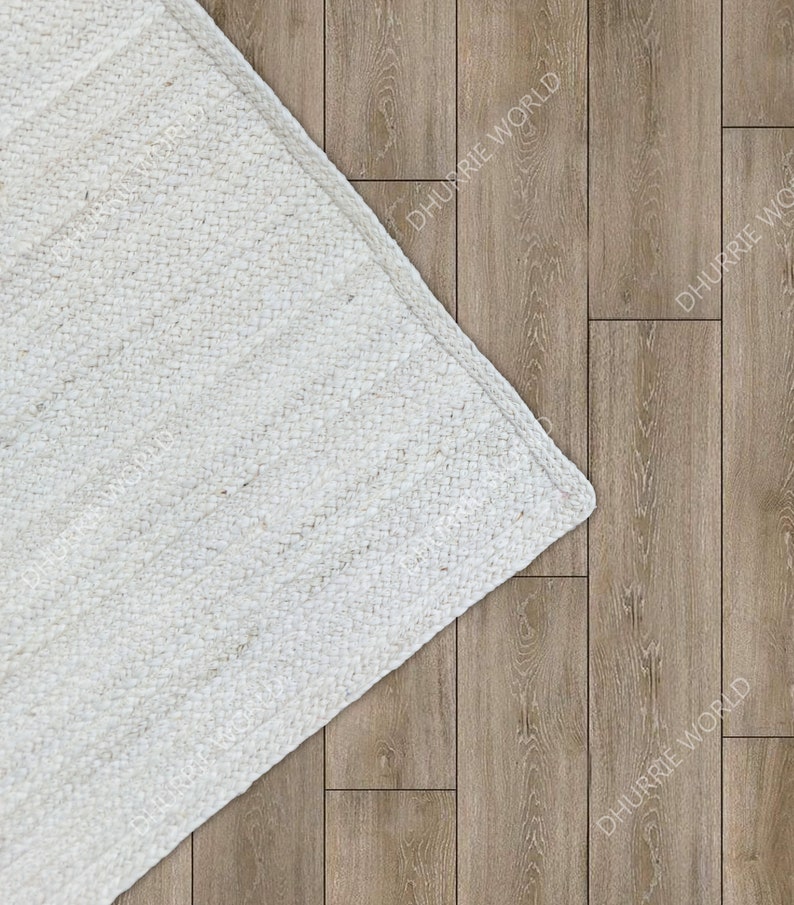 Op de afbeelding: Een wit geweven tapijt met een textuur. Het tapijt bedekt gedeeltelijk een houten vloer.