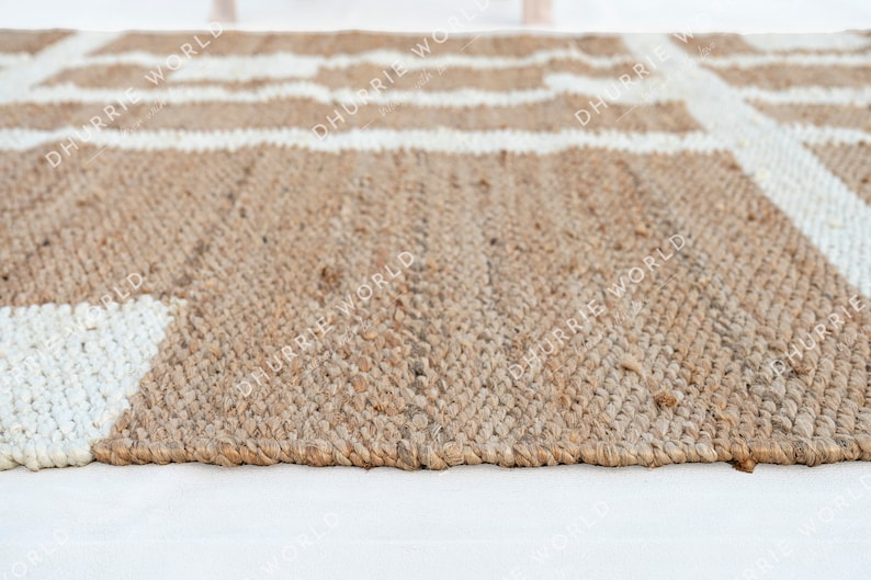 May include: Close-up of a natural fiber rug with a white geometric pattern. The rug is made of jute and has a natural, earthy tone.
