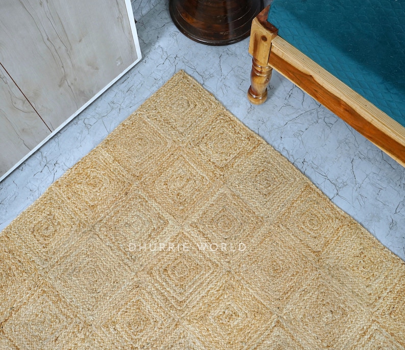 Puede incluir: Una alfombra de fibra natural con un patr&oacute;n cuadrado en color beige claro. La alfombra est&aacute; hecha de yute y tiene una superficie texturizada.