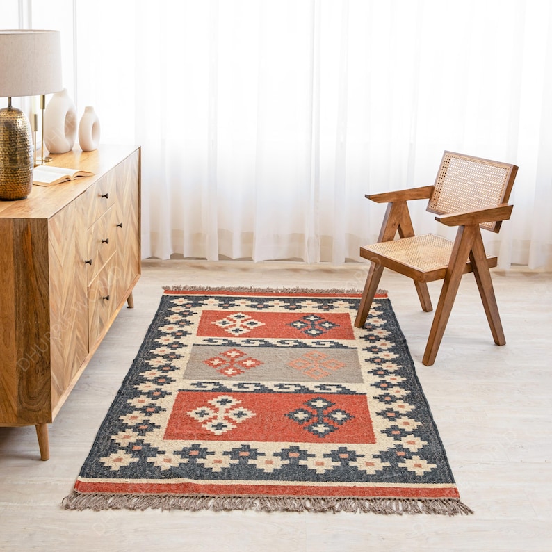 May include: A red, black, and beige patterned rug with a geometric design. The rug has a fringe border and is laid out on a wooden floor.