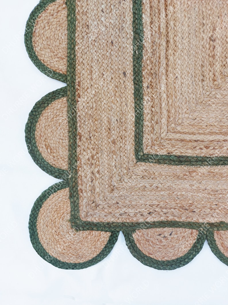 K&ouml;nnte beinhalten: Ein quadratischer Jute-Teppich mit gr&uuml;nem Rand und einem gewellten Saum. Der Teppich ist aus Naturfasern gefertigt und hat einen rustikalen Look.