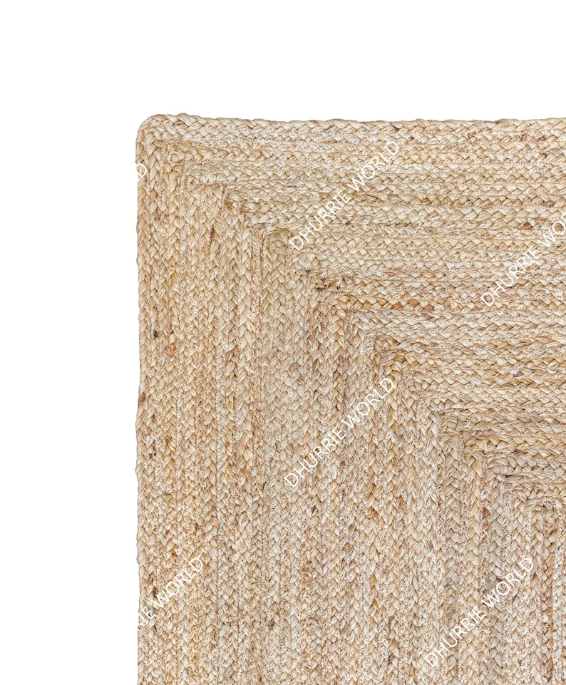 May include: A square natural jute rug with a woven pattern. The rug has a light beige color and a slightly rough texture.