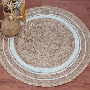 Puede incluir: Una alfombra redonda de yute con un borde blanco. La alfombra tiene una textura natural, tejida y un diseño sencillo.