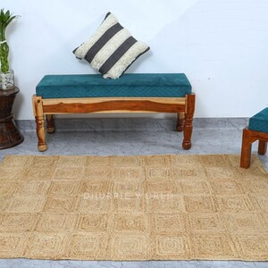 Puede incluir: Una alfombra de yute natural con un patr&oacute;n cuadrado de color marr&oacute;n claro. La alfombra se coloca delante de un banco de madera con un coj&iacute;n turquesa y un peque&ntilde;o taburete de madera con un coj&iacute;n turquesa.