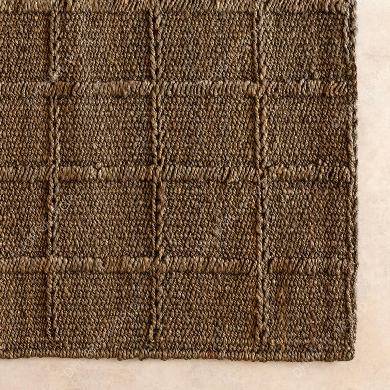 Puede incluir: Primer plano de una alfombra marr&oacute;n tejida con un patr&oacute;n de cuadr&iacute;cula. La alfombra est&aacute; hecha de fibras naturales, con una superficie texturizada y una paleta de colores neutros. El dise&ntilde;o presenta una serie de cuadrados y rect&aacute;ngulos.