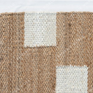 May include: A close-up of a natural fiber rug with a woven pattern. The rug has two white rectangular shapes in the center.