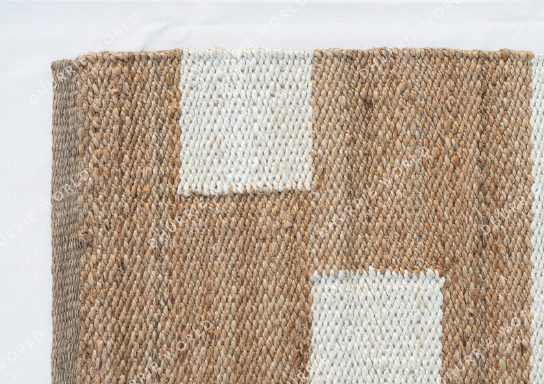 May include: A close-up of a natural fiber rug with a woven pattern. The rug has two white rectangular shapes in the center.