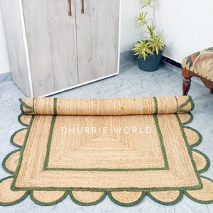 May include: A natural fiber rug with a green border and scalloped edges. The rug is rolled up and the text "DHURRIE WORLD" is visible in the center.