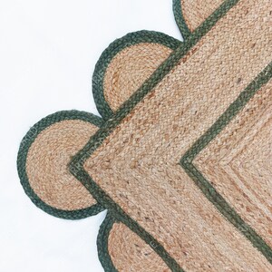 K&ouml;nnte beinhalten: Ein Jute-Teppich mit gr&uuml;nem Rand und gewellten Kanten. Der Teppich ist aus Naturfasern gefertigt und hat einen rustikalen Look.