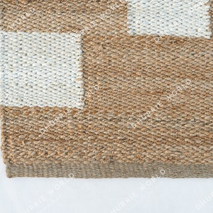 May include: A close-up of a natural fiber rug with a checkered pattern. The rug is made of woven jute and has a natural brown color with white squares.