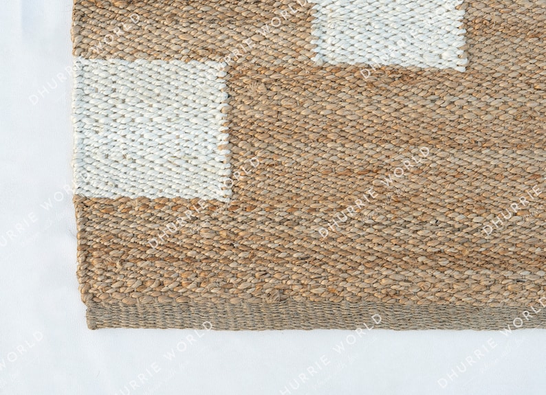 May include: A close-up of a natural fiber rug with a checkered pattern. The rug is made of woven jute and has a natural brown color with white squares.