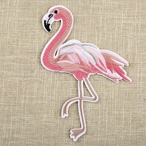 May include: Pink flamingo embroidered patch with a white outline. The flamingo is standing on one leg with its head bent back.