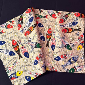 May include: A beige fabric runner with a repeating pattern of colorful fish and the text "Portuguesa Sardinha".