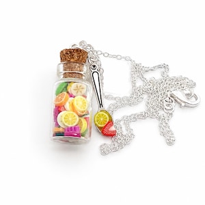 Könnte beinhalten: Eine silberfarbene Halskette mit einem kleinen, durchsichtigen Glasflaschenanhänger, der mit bunten Miniatur-Obstscheiben gefüllt und mit einem Korken verschlossen ist, sowie einem silberfarbenen Löffelanhänger mit Zitrone und Erdbeere.