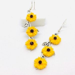Puede incluir: Un par de pendientes de aro de plata con tres colgantes de girasol amarillo en cada pendiente.