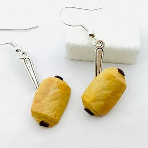 Könnte beinhalten: Ein Paar silberne Ohrringe mit einem Anhänger aus einem mit Schokolade gefüllten Gebäck. Das Gebäck ist hellbraun mit einer dunkelbraunen Schokoladenfüllung.