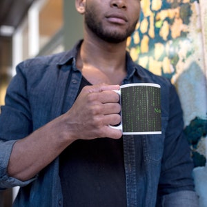 Może przedstawiać: Biały kubek ceramiczny z czarno-zielonym wzorem przedstawiającym kod w stylu macierzy i słowo "NaN".