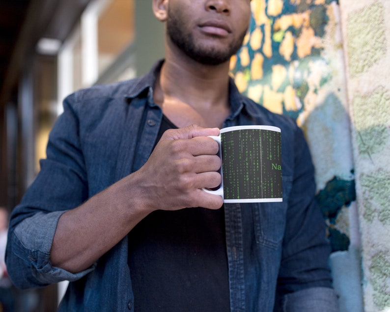 Może przedstawiać: Biały kubek ceramiczny z czarno-zielonym wzorem przedstawiającym kod w stylu macierzy i słowo "NaN".