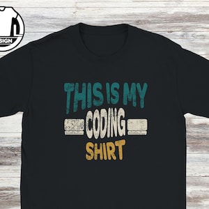 Puede incluir: Camiseta negra con el texto "THIS IS MY CODING SHIRT" en verde azulado, blanco y dorado. El diseño tiene un aspecto envejecido y vintage. La camiseta tiene cuello redondo y mangas cortas.