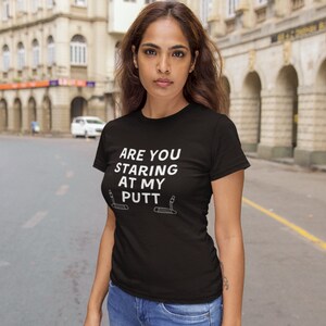 May include: A black t-shirt with white text that reads "Are you staring at my putt?" with two golf clubs on either side of the text.