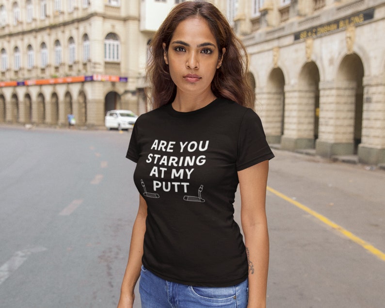 May include: A black t-shirt with white text that reads "Are you staring at my putt?" with two golf clubs on either side of the text.