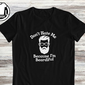 Puede incluir: Camiseta negra con un gráfico blanco de un hombre con barba y gafas. El texto dice "Don't Hate Me Because I'm Beardiful."