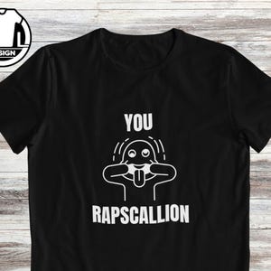 Op de afbeelding: Zwart T-shirt met een witte afbeelding van een cartoon gezicht met de tekst "You rapscallion".