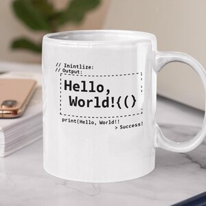 Peut inclure: Une tasse en céramique blanche avec une anse noire et le texte "But First, Coffee" en noir, en gras. La tasse est posée sur une surface blanche.
