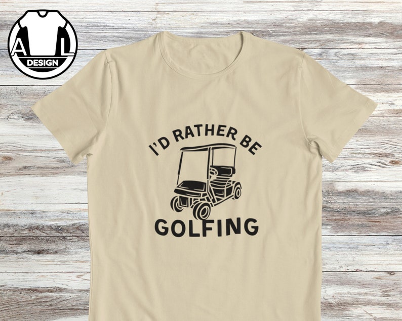 May include: A beige t-shirt with black text that reads "I'd rather be golfing" and a black silhouette of a golf cart.