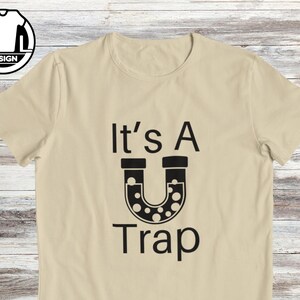 May include: A beige t-shirt with black text that reads "It's A U Trap" with a black illustration of a U-shaped pipe with black dots inside.