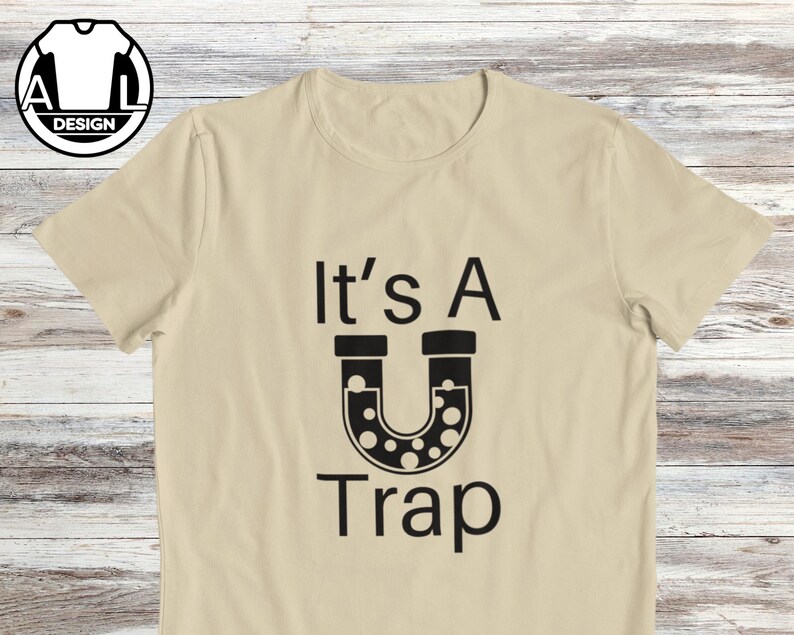May include: A beige t-shirt with black text that reads "It's A U Trap" with a black illustration of a U-shaped pipe with black dots inside.