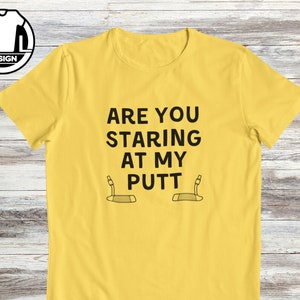 May include: Yellow t-shirt with black text that reads "Are you staring at my putt" with a golf putter graphic below the text.