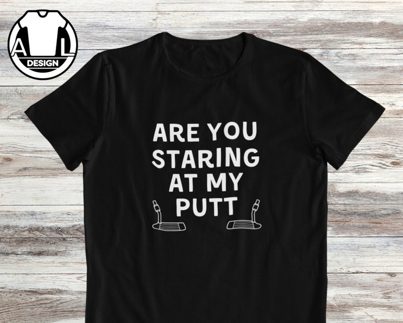 May include: Black t-shirt with white text that reads "Are you staring at my putt?" with a graphic of a golf putter below the text.