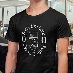 May include: A black t-shirt with a white graphic design that says "Sorry I'm Late I Was Coding" with a computer monitor, code, and gear icon.