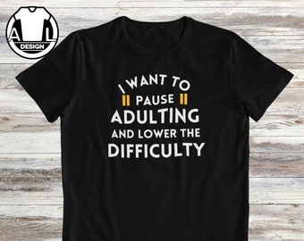 Puede incluir: Camiseta negra con texto blanco que dice "Quiero pausar la adultez y bajar la dificultad". El texto está rodeado por dos líneas paralelas amarillas.