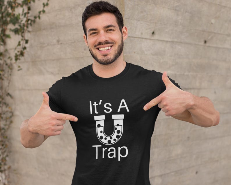 May include: A black t-shirt with white text that reads "It's A U Trap" with a graphic of a horseshoe magnet with black dots.