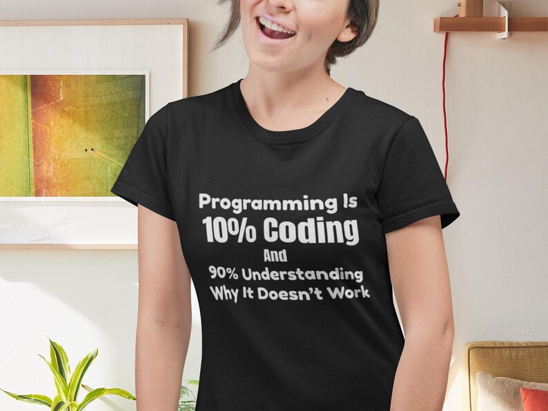 Op de afbeelding: Een zwart t-shirt met korte mouwen en witte tekst: Programming Is 10% Coding And 90% Understanding Why It Doesn't Work. Het shirt heeft een ronde hals en een standaard pasvorm, waarbij de bedrukte tekst duidelijk op de borst is weergegeven.