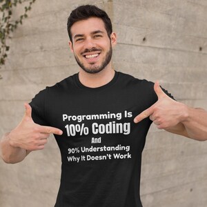 Op de afbeelding: Een zwart t-shirt met korte mouwen en witte tekst die luidt: Programming Is 10% Coding And 90% Understanding Why It Doesn't Work. Het shirt heeft een ronde hals en is gemaakt van effen zwarte stof met duidelijke, witte letters.